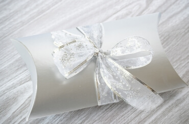 Silver pillow box wrapped with white and silver ribbon with cinnamon roasted pecan inside